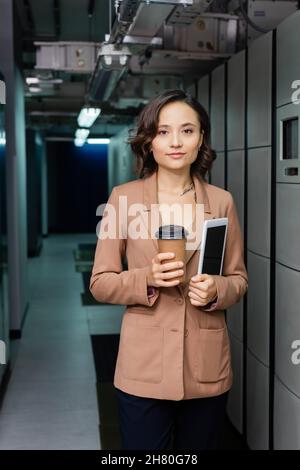 young engineer with paper cup and digital tablet looking at camera in data center Stock Photo