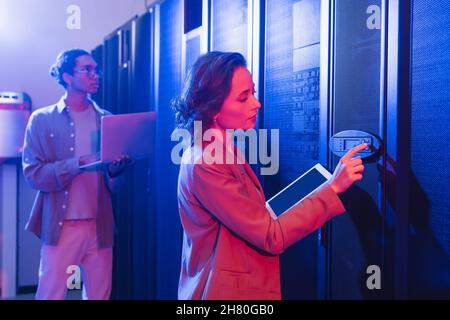 young engineer with digital tablet checking server near african american colleague with laptop Stock Photo