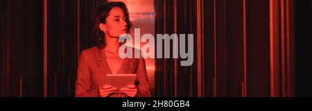 young woman with digital tablet looking at servers in data center with neon light, banner Stock Photo