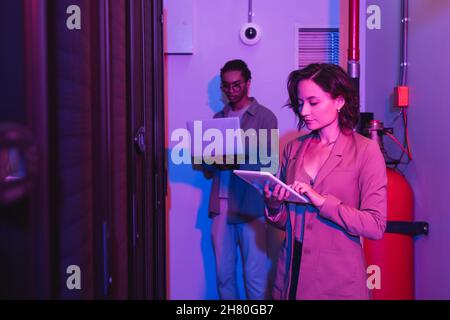 interracial programmers using gadgets while working in data center in neon light Stock Photo
