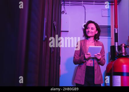 young programmer holding digital tablet and smiling while working in data center Stock Photo