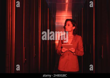 engineer with digital tablet looking at servers in data center with neon light Stock Photo