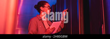 african american technician with digital tablet checking server in data center in neon light, banner Stock Photo