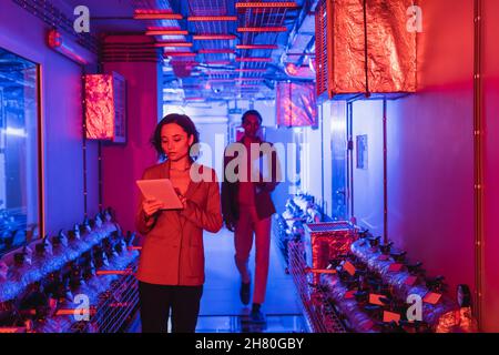 young programmer using digital tablet near blurred african american colleague in technical equipment room Stock Photo