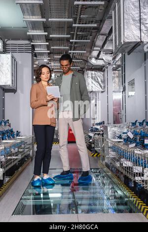 multiethnic engineers looking at digital tablet near cooling system in data center Stock Photo