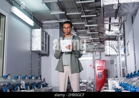 young afican american engineer using digital tablet while standing near cooling system  of data center Stock Photo