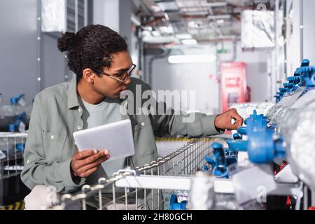 african american engineer with digital tablet checking cooling system in technical equipment room of data center Stock Photo