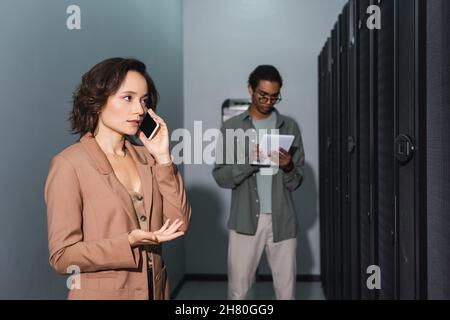 engineer talking on mobile phone near blurred african american colleague with digital tablet in data center Stock Photo