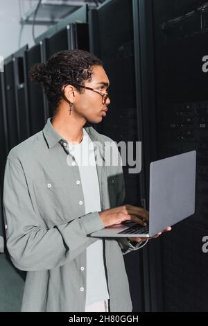 young african american programmer using laptop while working with servers in data center Stock Photo