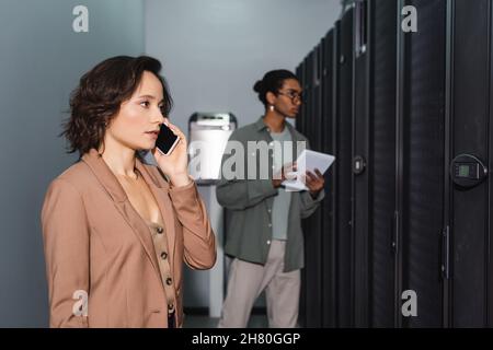 engineer talking on smartphone near blurred african american programmer with digital tablet Stock Photo
