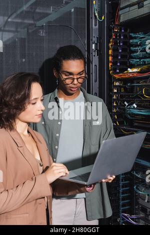 multiethnic technicians working on laptop near server in data center Stock Photo