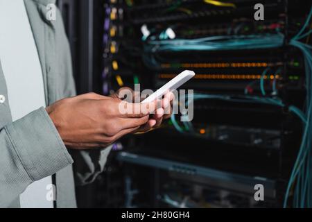 cropped view of african american engineer using smartphone near server in data center Stock Photo