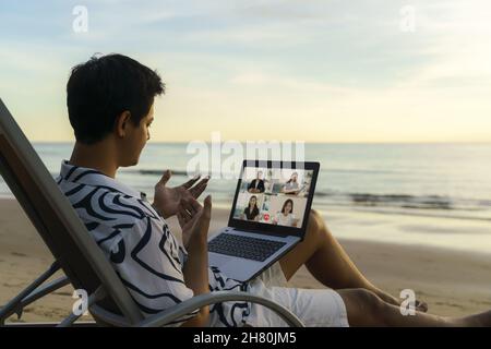Asian business man having remote video conference call with his business team at the beach during vacation in holiday. Stock Photo