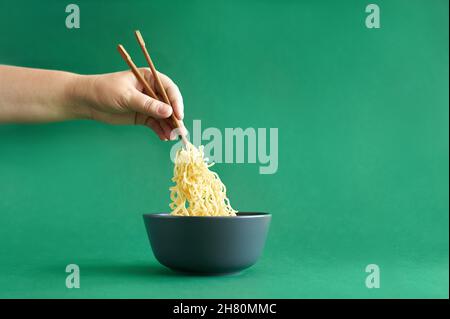 Female hand holding chopsticks with noodle in the dark grey bowl on green Stock Photo