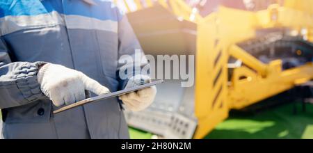 Banner industrial senior engineer in hardhat is using tablet computer in construction site background bulldozer, sunlight. Stock Photo