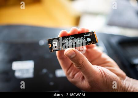 Banner Elk, USA - June 23, 2021: Macro closeup of hand holding Crucial micro chip by Micron and laptop computer keyboard for replacing dead hard drive Stock Photo