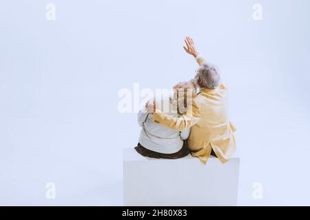 Back view of two people, senior woman and bearded man in retro style clothes, fashion of 70s, 60s years sitting together isolated on white studio Stock Photo