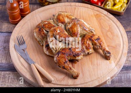 Tapaca (tabaca) chickens with cherry tomatoes and pepperoni on a wooden board. Traditional Georgian dish. Close-up. Stock Photo