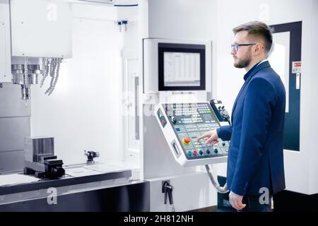 Worker man entering data in CNC machine at automatic factory floor. Modern process metal detail production going for car. Stock Photo