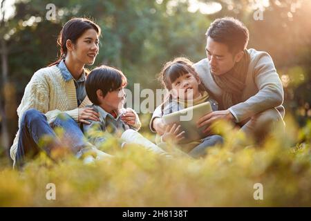 asian family with two children relaxing outdoors in city park Stock Photo