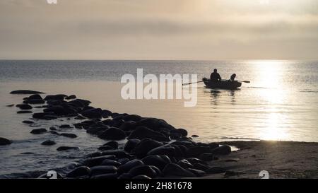 A rowing boat heading out into sea high contrast against the sun Stock Photo