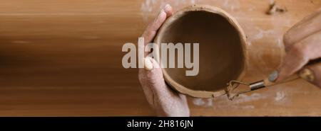 pottery in workshop clay art concept. close-up on the hands of a young ceramist with an unbaked clay pot. artisan hands hold a clay cup Stock Photo
