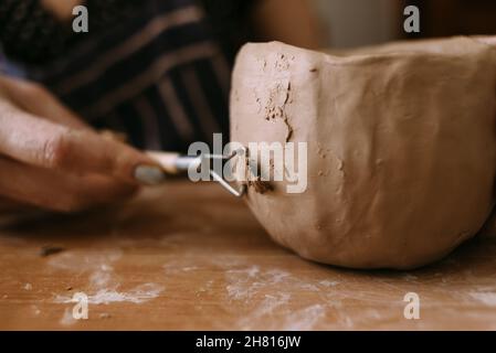 Close-up of an earthenware bowl and female hands decorate a ceramic product with a special tool. Potter's creative workshop. handicraft concept Stock Photo