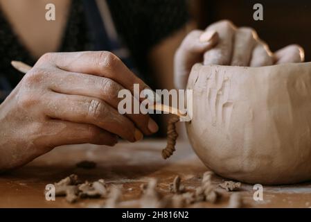 A sculptor makes a plate from a cast. woman potter working with clay brush hands close-up. applies a pattern to the product. Stock Photo