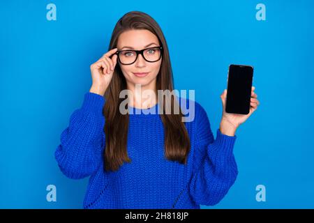 Portrait of attractive trendy content girl holding in hand device gadget touching specs promo isolated over bright blue color background Stock Photo