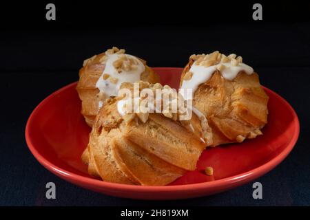 Round eclair in a red plate on the table. Food on a black background Stock Photo