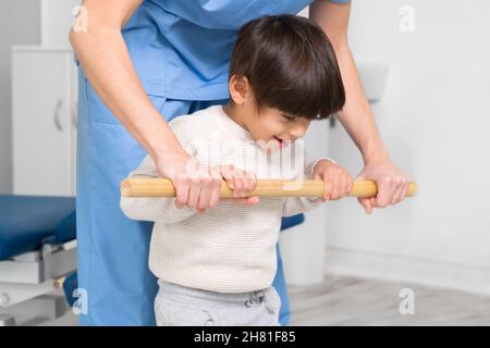 Physiotherapist and kid walking in rehabilitation center. Doctor supports a children with cerebral palsy during physiotherapy treatment. High quality photo. Stock Photo