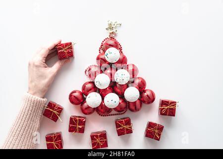 A female hand holds a Christmas present. On a white background, a Christmas tree made of white and red balls with gifts. Festive postcard. Stock Photo