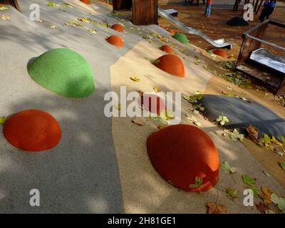 playground. public park.colorful orange, yellow and green rubber safety flooring of playful semi spheres. shiny stainless steel slide in a distance. Stock Photo