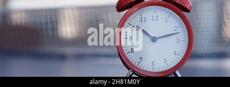 Red alarm clock standing on tennis table closeup Stock Photo