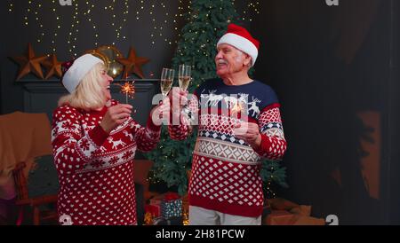 Smiling elderly grandparents family couple holding Christmas bengali sparkles, glasses of champagne Stock Photo