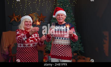 Smiling senior grandparents family couple holding Christmas bengali sparkles, glasses of champagne Stock Photo