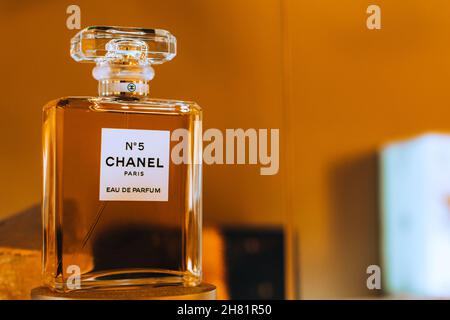 Display of glass bottle Chanel No. 5 perfume by French luxury brand Chanel against the golden background. Famous female fragrance. Stock Photo