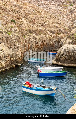 Boats and luzzus - traditional wooden colorful fishing boats -moored in the very end of Wied iż-Żurrieq inlet among cliffs. Stock Photo