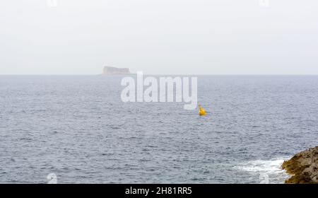 Yellow steel navigational floating buoy - Special Mark - in the blue Mediterranean with a vague Filfla island at the horizon. Stock Photo