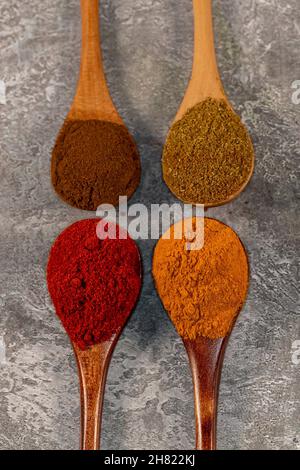 Looking down at wooden spoons filled with colourful spices, against a grey background Stock Photo