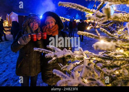 Breitnau, Germany. 26th Nov, 2021. Ursula Baumann (l-r) and Manuela Mohr stand with two cups of mulled wine in their hands at the Christmas market in Ravenna Gorge. It is open on all four Advent weekends and under strict Corona protection regulations. Credit: Philipp von Ditfurth/dpa/Alamy Live News Stock Photo