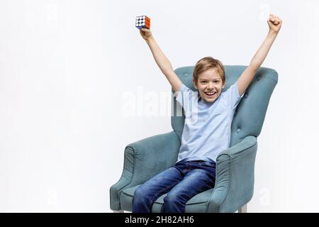 Kyiv, Ukraine, October 9 2021: Young boy holding Rubik's cube and lifting arms with joy. Child expressing happiness after solving mental puzzle. Stock Photo
