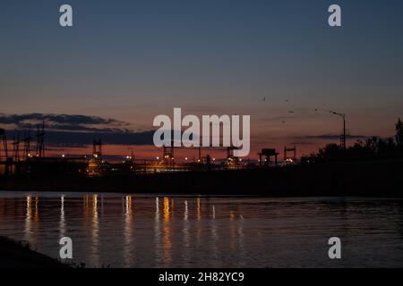 Dam at night. Concrete dam on the river. Night city with lights at beautiful sunset Long exposure view dam and city on sunset, vivid, blurry Stock Photo