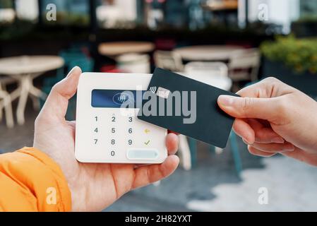 Crop unrecognizable female customer with credit card making contactless payment on POS terminal in street cafe Stock Photo