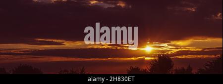 The rays of the setting sun make their way through the cloudy sky. Stock Photo
