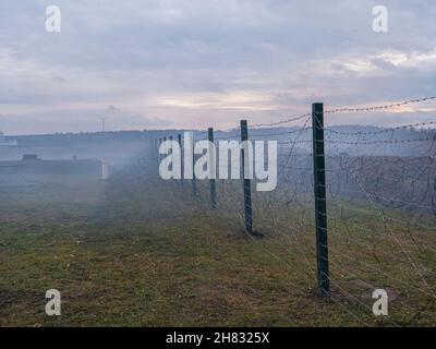 Rows of barbed wire on the state border. The separation of the two countries. Foggy autumn landscape  Stock Photo