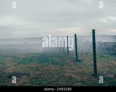 Rows of barbed wire on the state border. The separation of the two countries. Foggy autumn landscape  Stock Photo