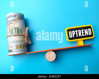 Block cylinder center between banknotes and word UPTREND on a blue background. Business concept. Stock Photo