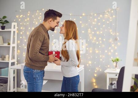 Couple in love standing, holding Valentine gift, looking at each other and smiling Stock Photo