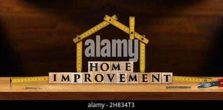 Wooden desk with a wooden folding ruler in the shape of a house with work tools and the text Home Improvement, made of wooden blocks. Stock Photo